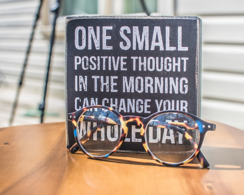 Photo of a piece of decor that says 'one small positive thought in the morning can change your whole day' with glasses in front of it.